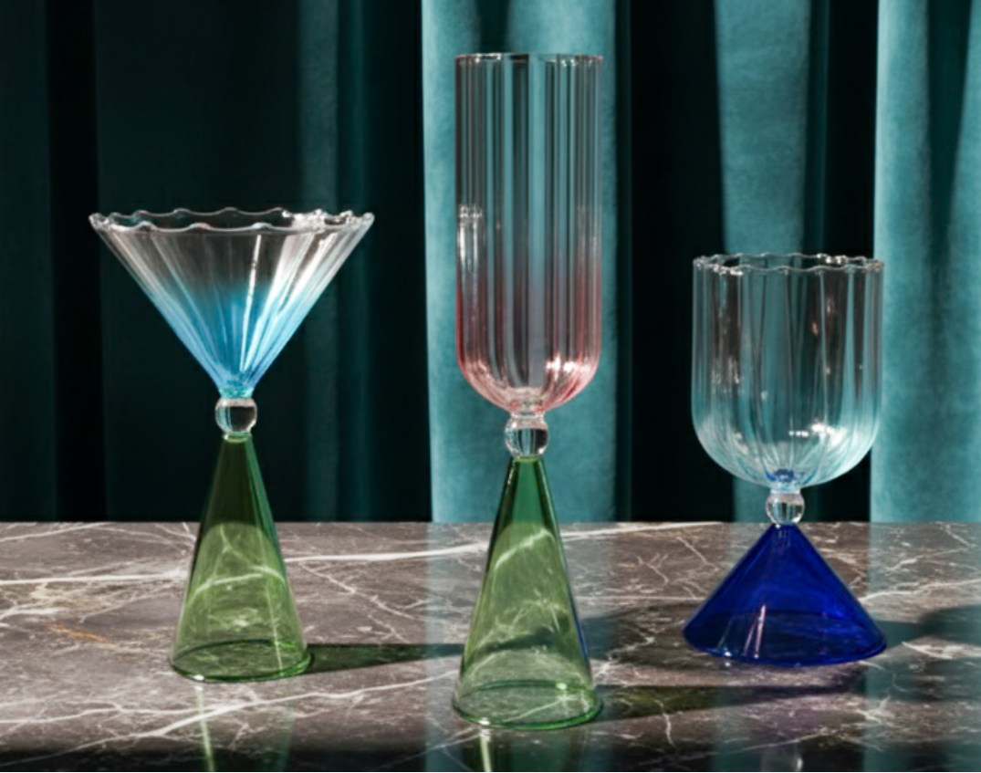 Three colorful glass goblets on a marble surface with a teal curtain background