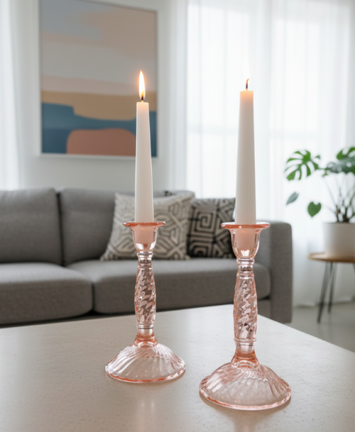Two  vintage pink swirl candle holders with white candles on a table in a living room.